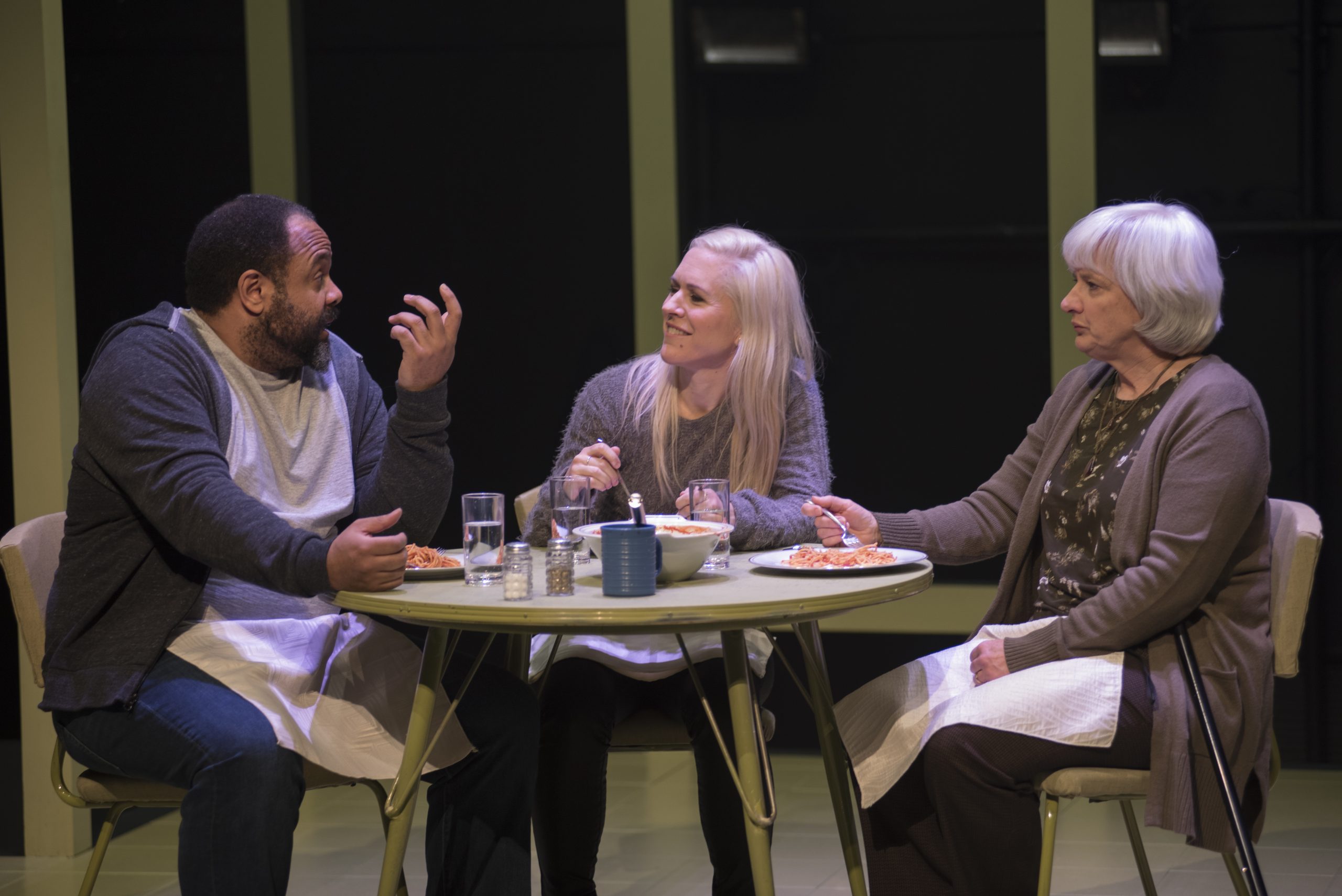 three people sit at a table in a play eating