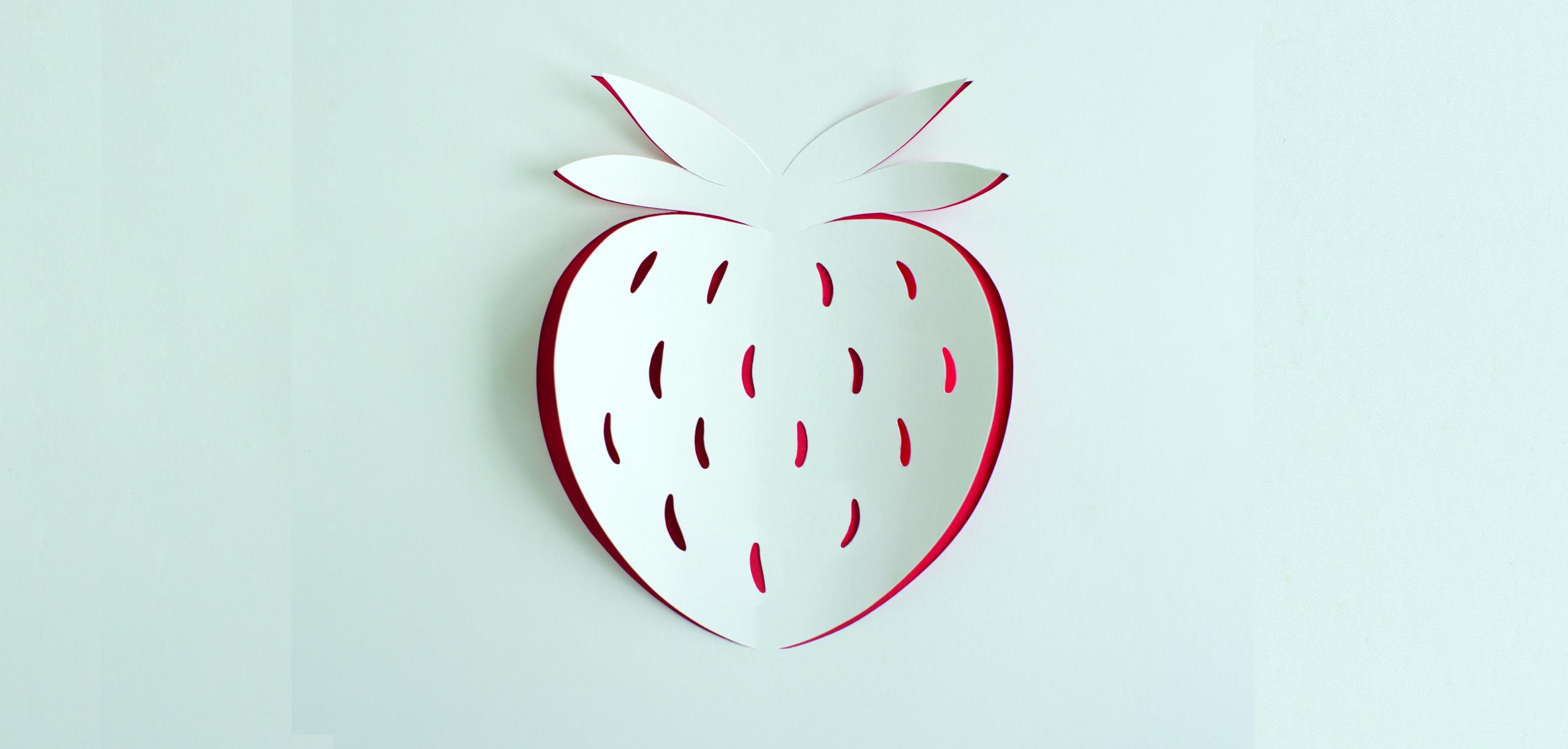 A strawberry design on white paper with red under the cut out strawberry design